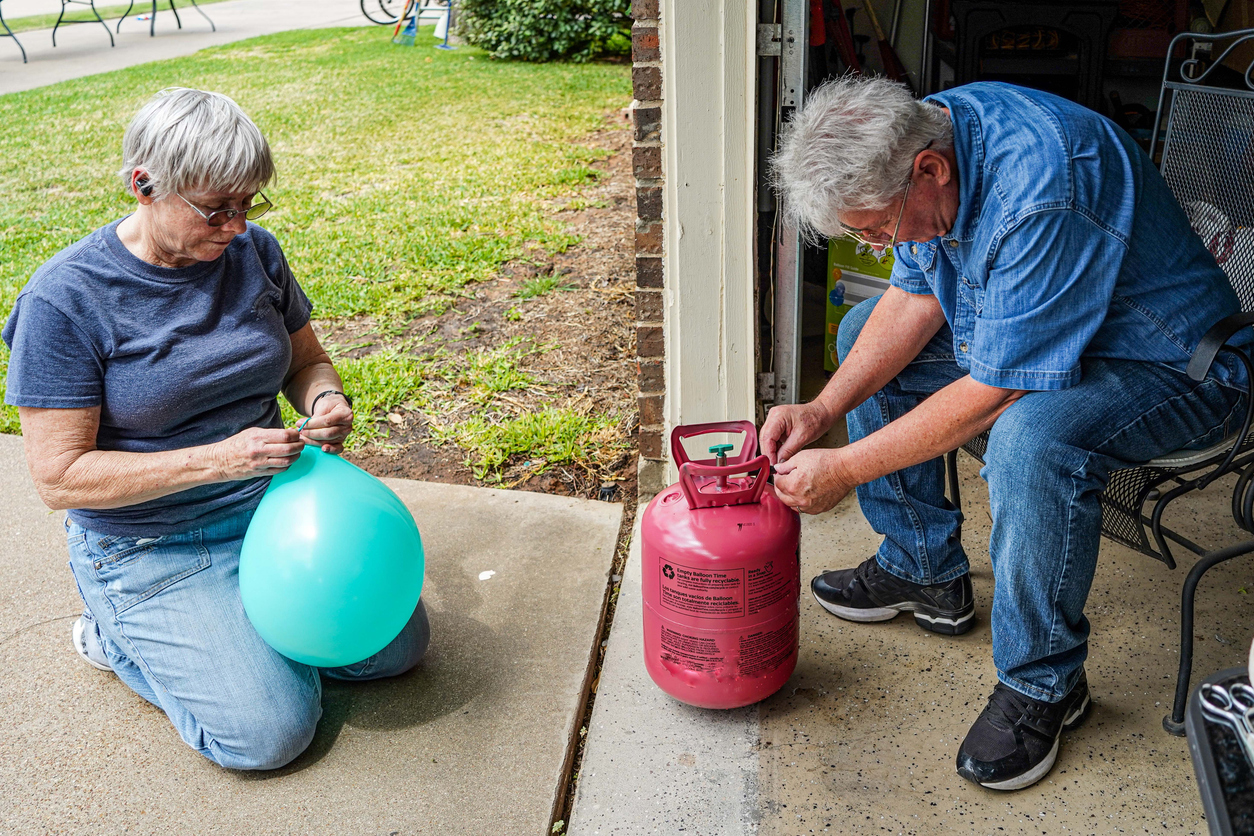 A senior man and woman fill balloons with helium gas from a helium tank for a special occasion.