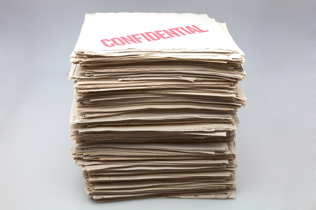 Dozens of pieces of paper are stacked into a pil with the work confidential types across the top piece of paper.