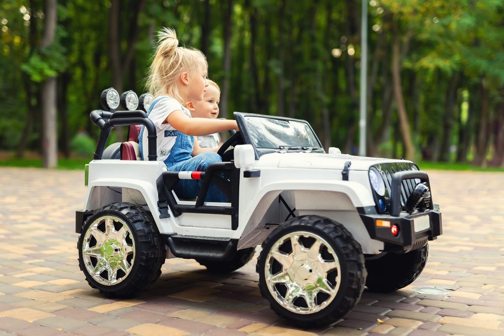 Two cute adorable blond sibings children having fun riding electric toy suv car in city park. Brother and sister enjoy playing and driving battery vehicle on city street outdoor. 